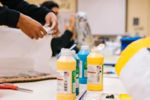 Hands working with paint bottles in a workshop setting, showcasing creative preparation for Project Titan's design and fabrication.